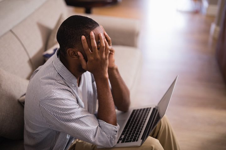 Black man sitting down and covering his face with a laptop in his lap - chronic sex addiction