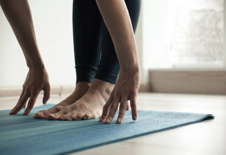 close up of hands and feet of person standing and stretching on yoga mat - through yoga
