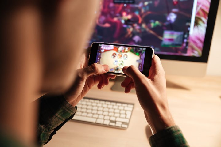 closeup of someone playing game on mobile phone in front of computer - gaming