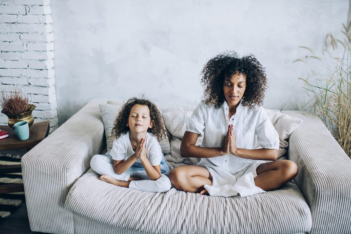 woman and her young daughter sitting on couch meditating at home - meditate